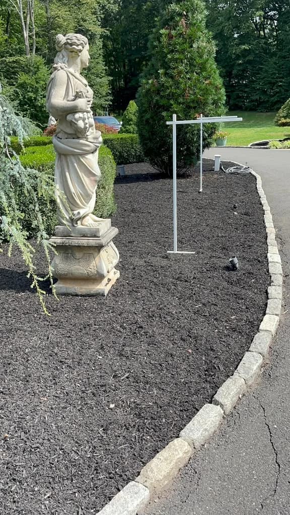 Long curved residential bed refreshed with dark mulch and stone edging