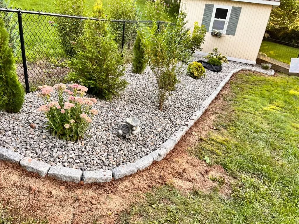 Curved residential garden bed finished with decorative stone and block edging