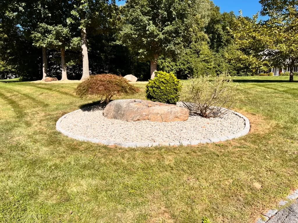 Circular front-yard landscape island finished with decorative rock and boulders