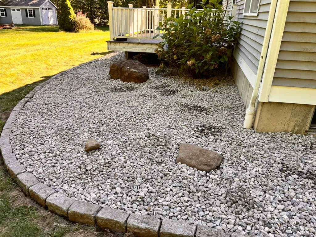 Side-yard foundation bed finished with decorative stone and a curved block border