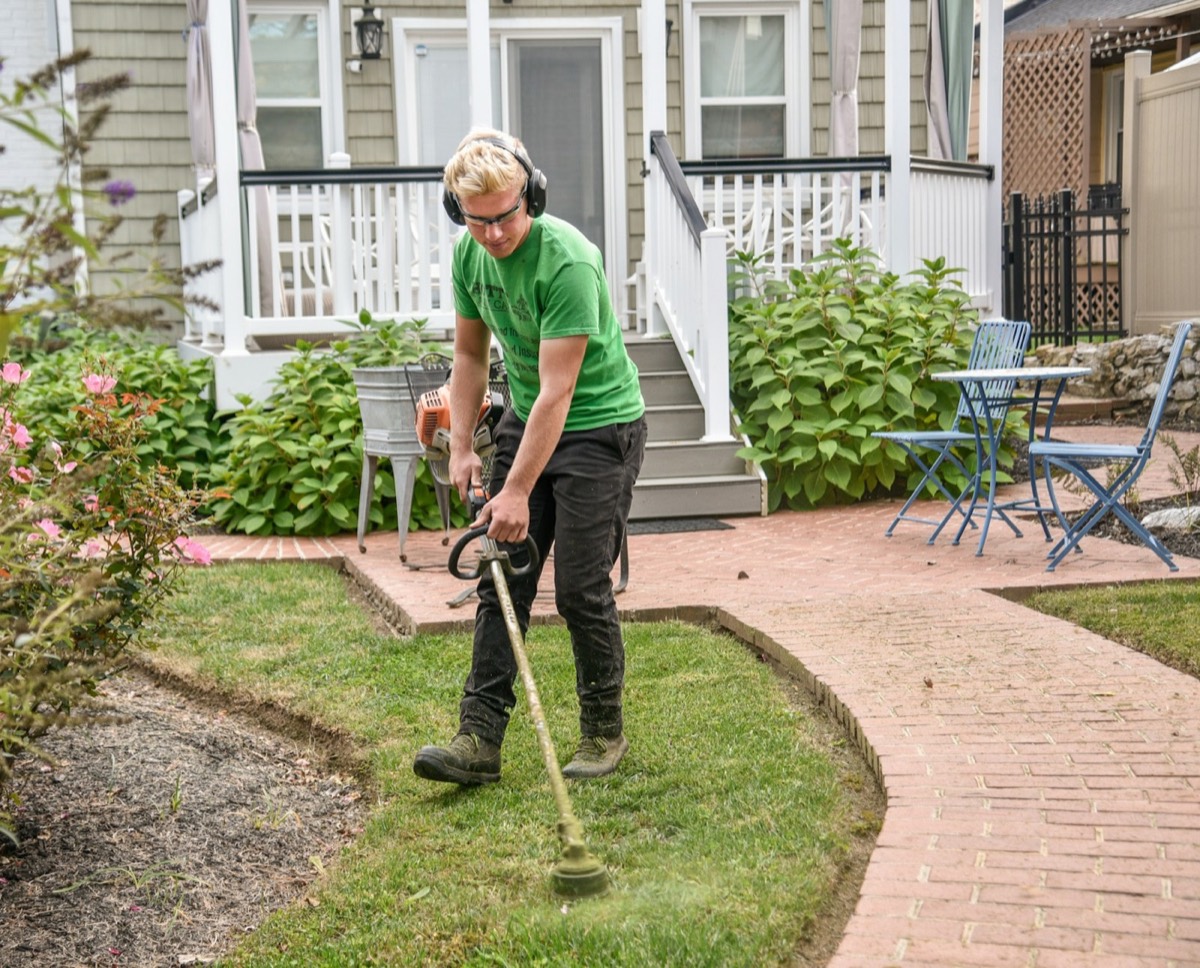 Landscaper trimming grass around a residential garden bed